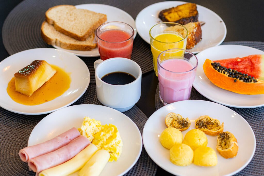 Mesa de café da manhã bem servida com café, sucos, pão de queijo, frutas e frios. Produção de conteúdo para redes sociais de hotéis.