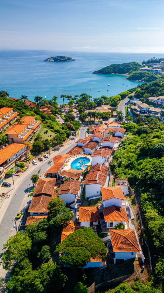 Fotografia aérea de drone mostrando uma pousada com telhados de barro, piscina central e vista para o mar. Fotografia imobiliária e turística.