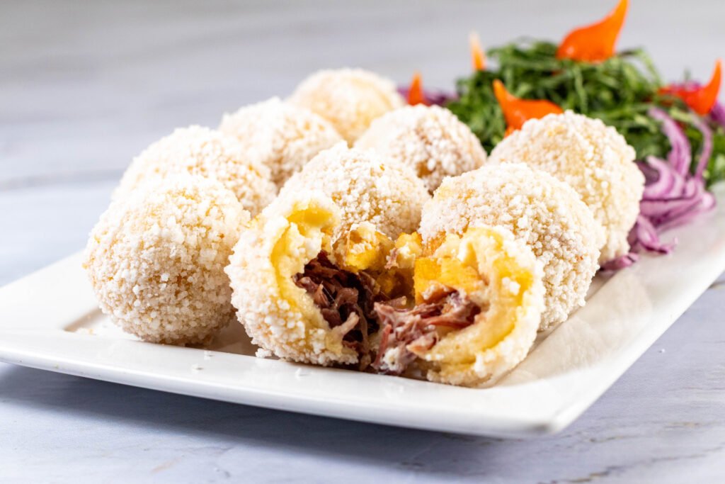 Bolinhos fritos crocantes recheados com carne seca e queijo, acompanhados de salada de folhas. Fotografia comercial para bares e restaurantes em Lauro de Freitas.