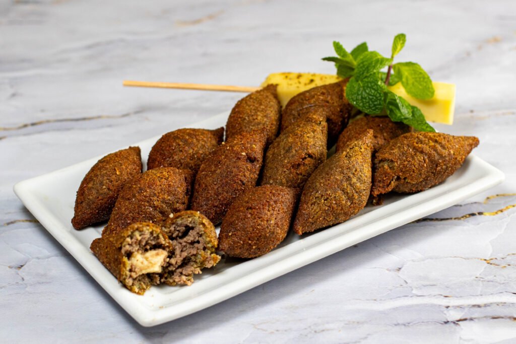 Prato branco com porção de quibes fritos recheados com queijo e carne, decorados com hortelã. Fotografia profissional para restaurantes e lanchonetes em Lauro de Freitas e Salvador.